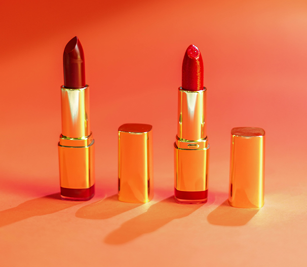 Four lipsticks in varying shades of red and orange on a gradient background